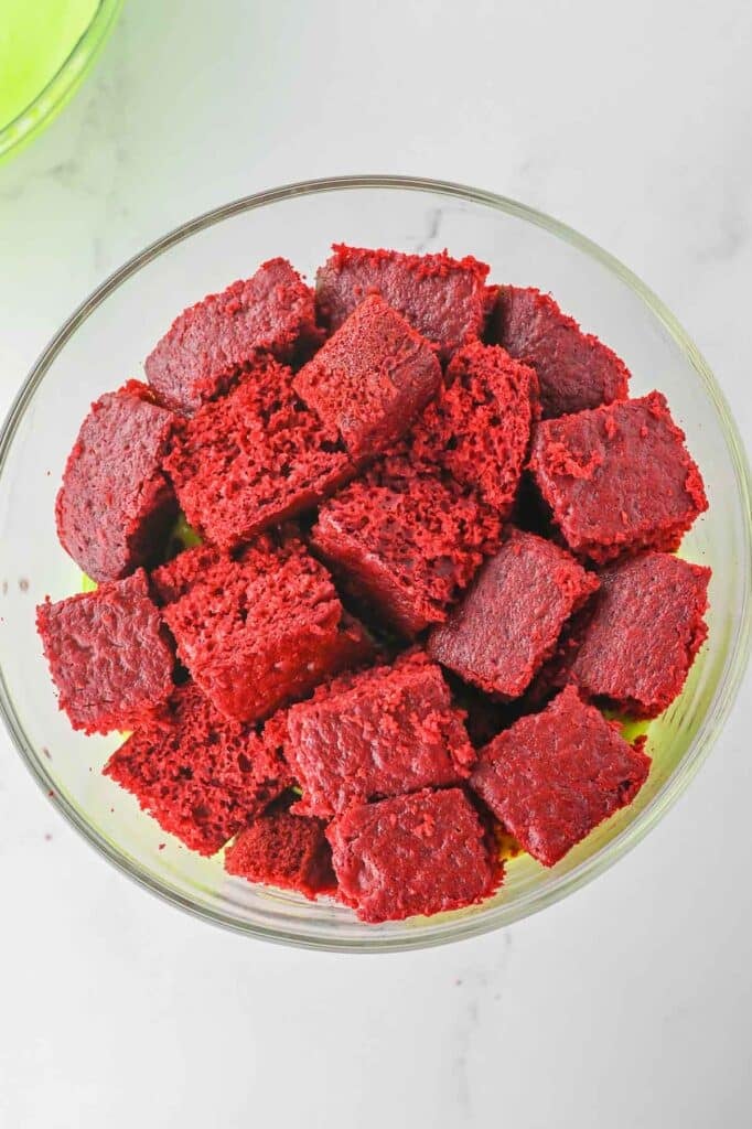 A bowl filled with cubed pieces of red velvet cake on a white marble countertop.