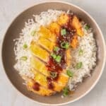 A bowl of white rice topped with air fryer chicken, drizzled with a katsu sauce and garnished with green onions.