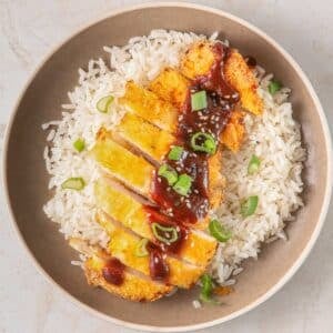 A bowl of white rice topped with air fryer chicken, drizzled with a katsu sauce and garnished with green onions.