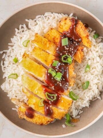 A bowl of white rice topped with air fryer chicken, drizzled with a katsu sauce and garnished with green onions.