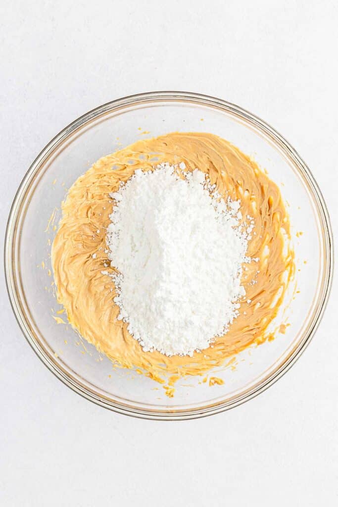 A glass bowl contains creamy peanut butter with a mound of powdered sugar in the center.