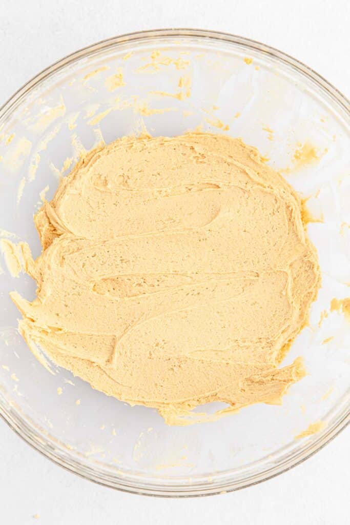 A glass bowl containing smooth, creamy peanut butter frosting mixture.