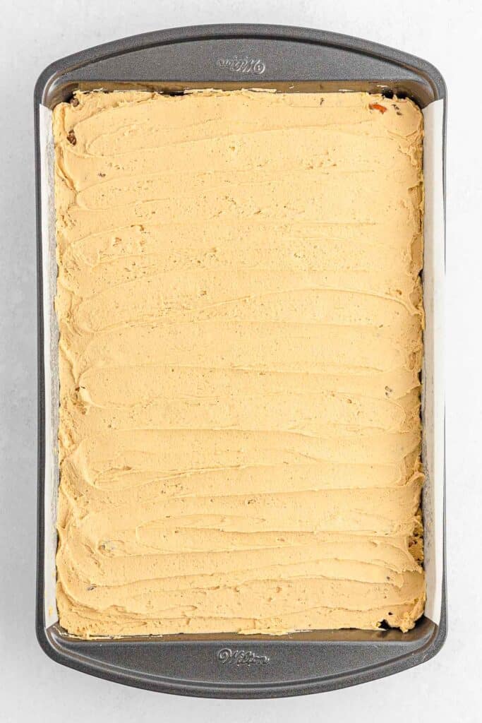 A rectangular baking tray spread with a smooth peanut butter frosting layer over the chocolate krispie base.