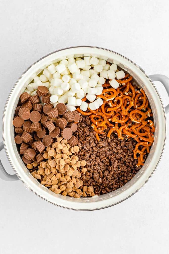A pot containing mini marshmallows, mini peanut butter cups, pretzels, cocoa krispies and peanut butter chips.