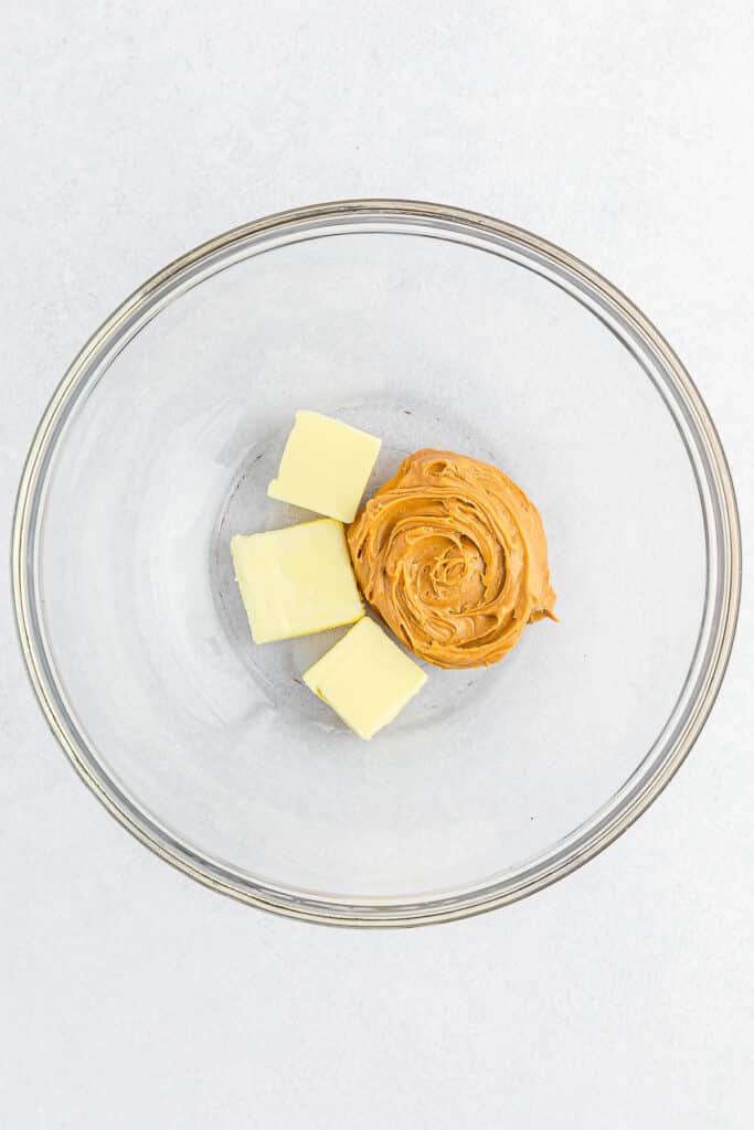 A glass bowl containing three butter cubes and a dollop of peanut butter.