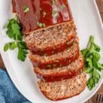 A glazed lipton french onion meatloaf partially sliced on a white platter, garnished with parsley.