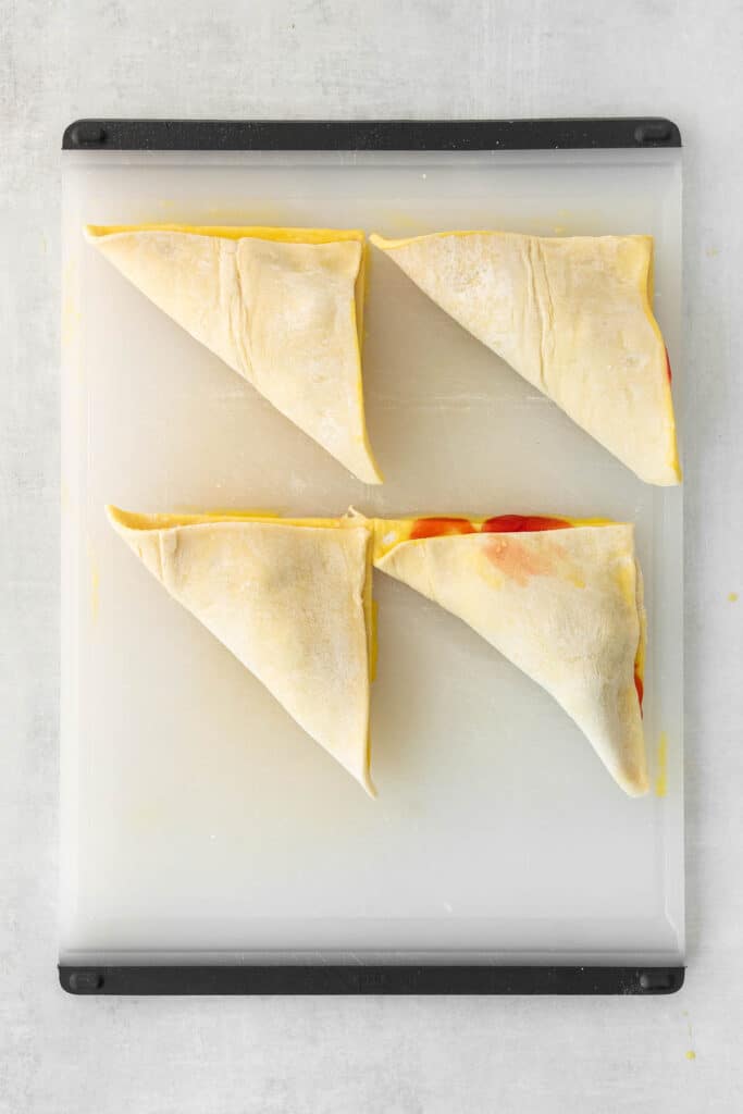 Four uncooked triangular puff pastries filled with cherry filing placed on a white cutting board.