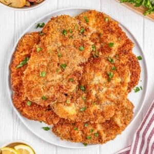 A plate of several golden-brown, breaded Milanesa steak garnished with parsley.