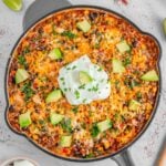 A skillet filled with mexican beef and rice topped with melted cheese, avocado, and a dollop of sour cream.