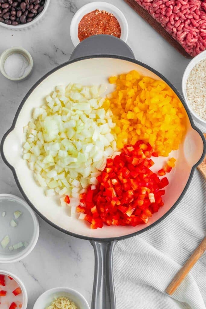 Chopped onion, yellow bell pepper, and red bell pepper in a pan.