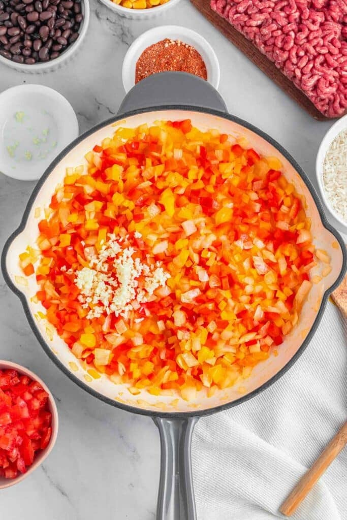 A pan with chopped yellow and red bell peppers with onions and garlic.