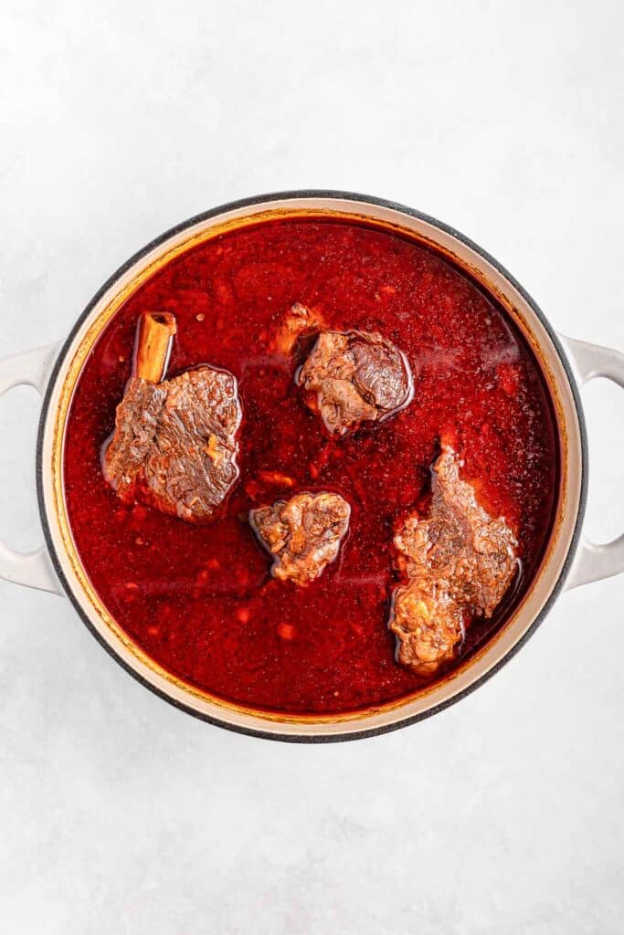 A pot filled with beef short ribs cooked in a rich red sauce.