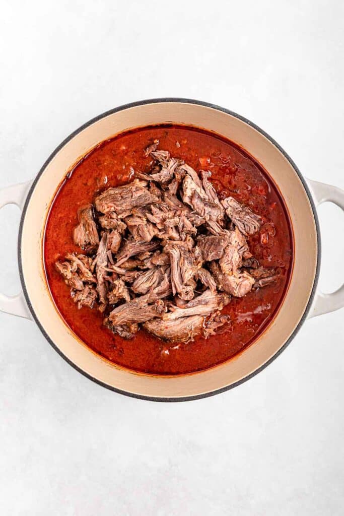 Shredded short rib in a red sauce inside a large pot.