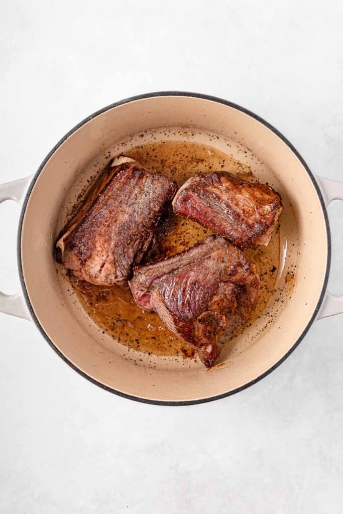 Three pieces of browned beef short ribs in a round pot.
