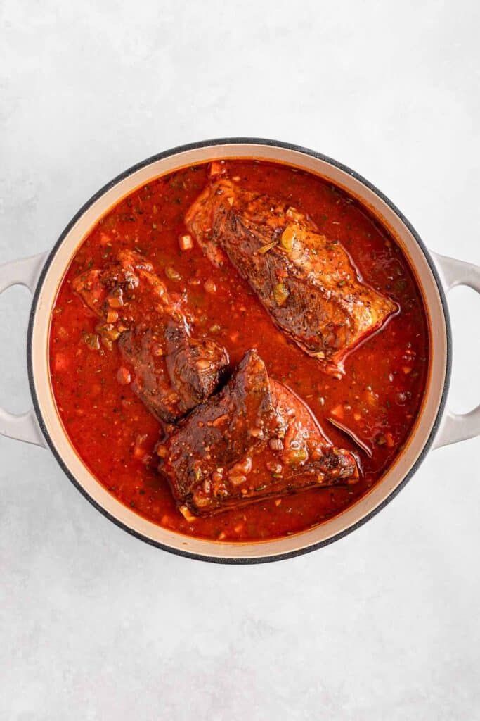 A pot filled with beef short ribs cooked in a rich red sauce.