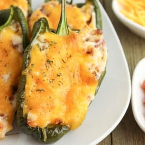 Stuffed poblano peppers topped with melted cheese on a white plate, with a side of grated cheese visible.