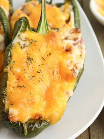 Stuffed poblano peppers topped with melted cheese on a white plate, with a side of grated cheese visible.