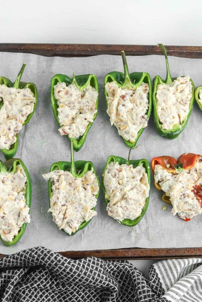 Halved poblano peppers filled with a creamy mixture are lined up on a baking sheet, ready for cooking.