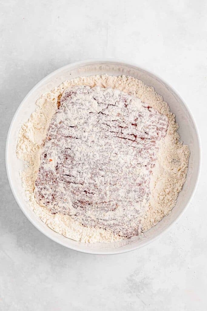 Beef steak coated in flour in a white bowl.