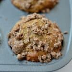 A freshly baked muffin in a muffin tray, topped with crumbly streusel pieces.