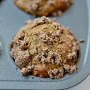 A freshly baked muffin in a muffin tray, topped with crumbly streusel pieces.