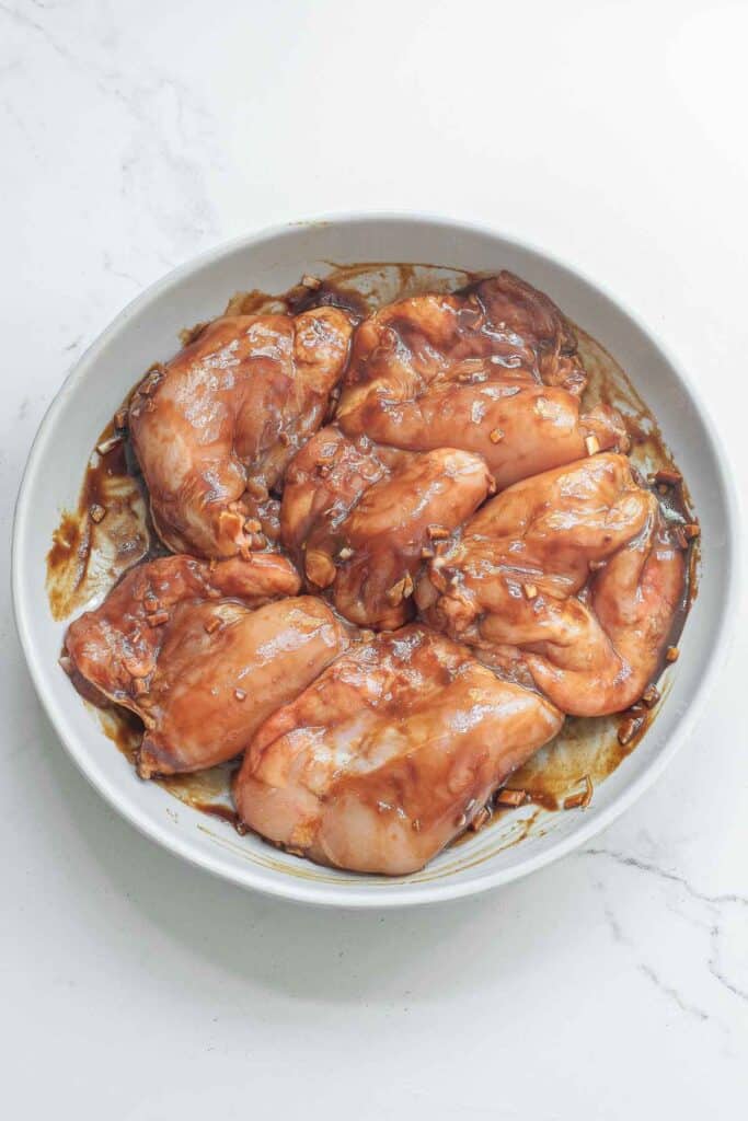 Raw chicken coated in a miso marinade on a white bowl on a marble surface.