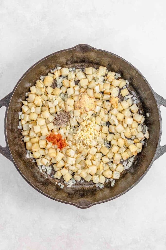 Diced potatoes and onions with spices in a cast iron pan.