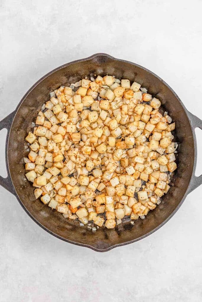 Diced potatoes sautéed in a cast iron skillet on a light gray surface.