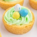 A Easter basket cookie cup filled with green icing, topped with three candy eggs: one blue, one yellow, and one speckled.