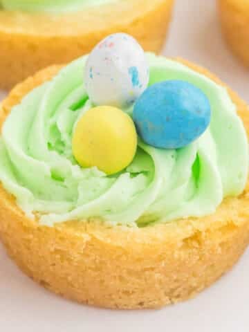 A Easter basket cookie cup filled with green icing, topped with three candy eggs: one blue, one yellow, and one speckled.