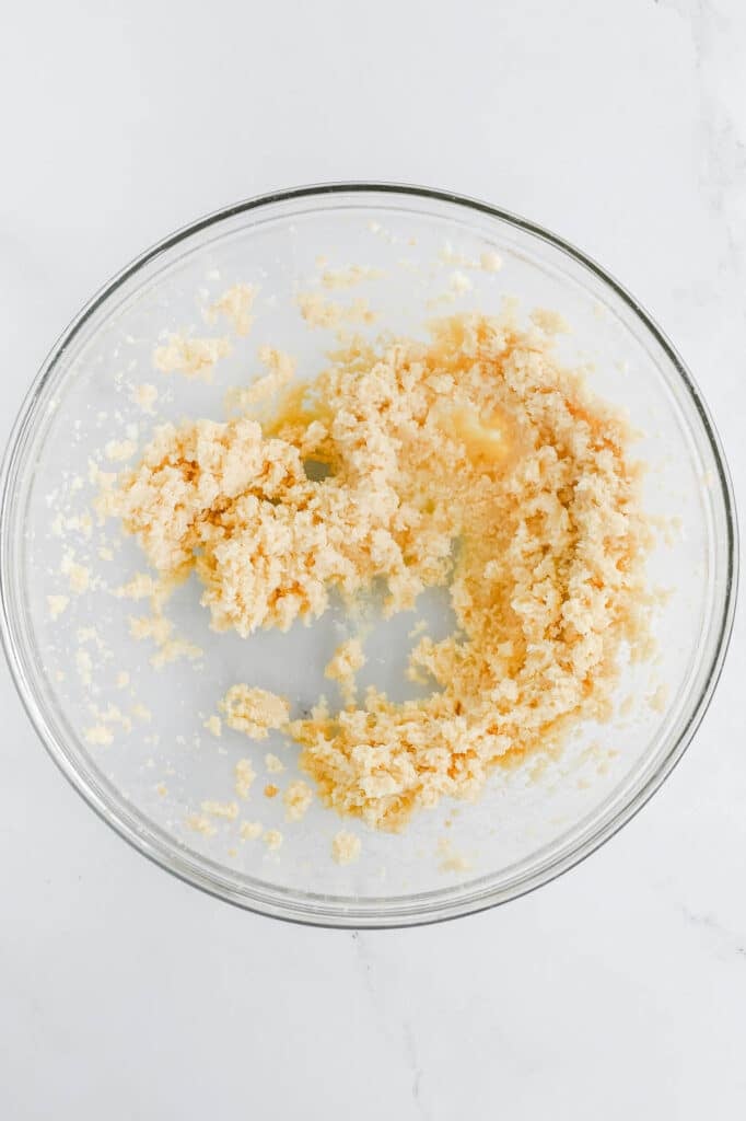 A glass bowl containing a mixture of butter and sugar, partially creamed together, on a white marble surface.