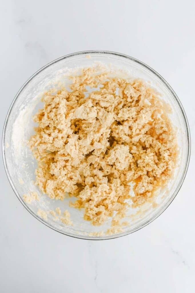 A glass bowl containing mixed cookie dough on a white countertop.