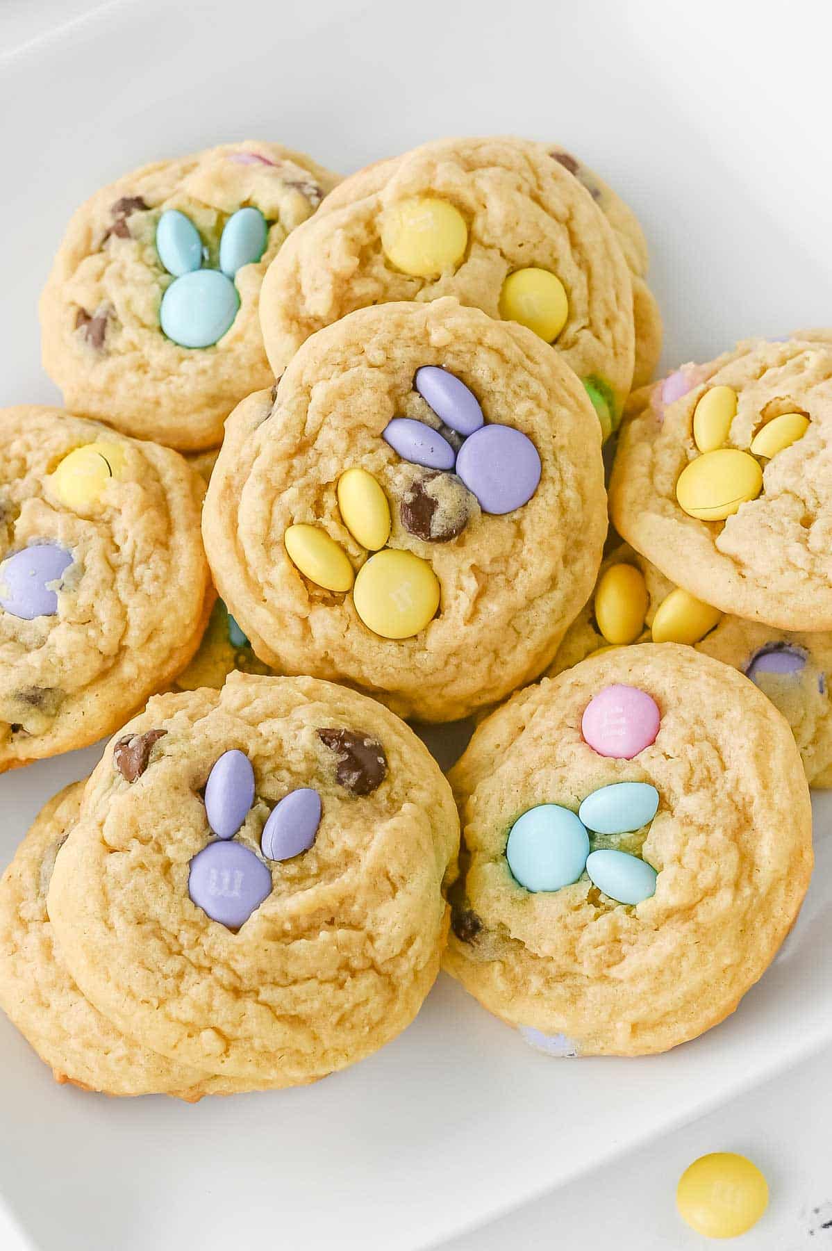 Plate of Easter cookies with pastel colored M&M candy and some with bunny shapes , on a white plate.