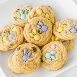 Easter cookies with pastel-colored M&M candies in shapes of bunny head with ears on a white plate.