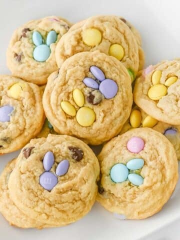Easter cookies with pastel-colored M&M candies in shapes of bunny head with ears on a white plate.