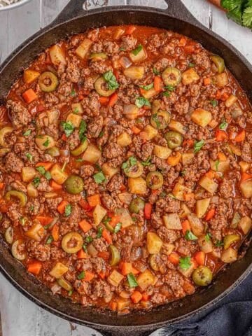 A skillet with Mexican Picadillo topped with cilantro on a grey table ready to be served.