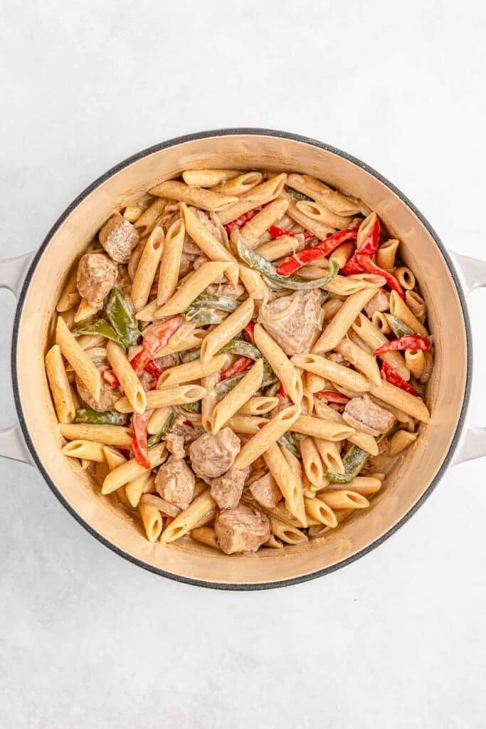 A pot of penne pasta mixed with chunks of chicken, red and green bell peppers, and a creamy sauce.