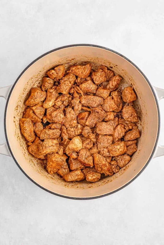 Seasoned diced chicken in a round pot on a light surface.