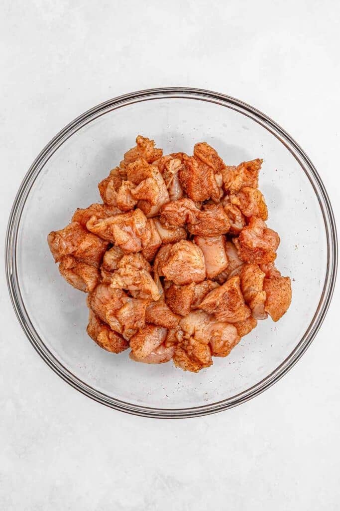 Diced raw chicken seasoned jerk seasoning in a clear glass bowl.