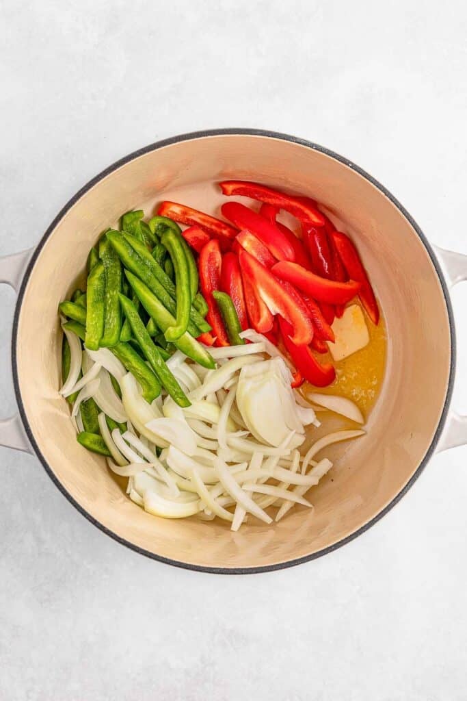 Sliced green peppers, red peppers, and onions in a dutch oven.