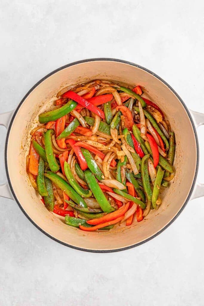 A pot filled with cooked sliced red and green bell peppers and onions on a light background.