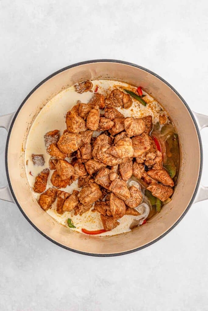 A pot filled with cooked chicken in a creamy sauce, mixed with red and green peppers.