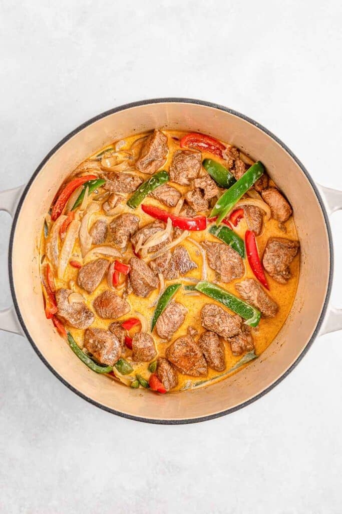 A pot containing chicken with sliced red and green peppers, onions, and a creamy sauce.
