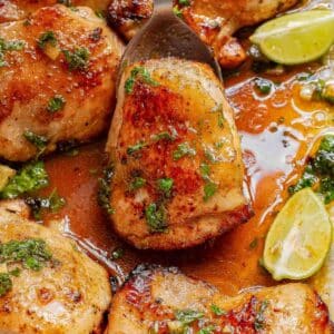 Close-up of cooked cilantro lime chicken thighs recipe in a flavorful sauce with herbs and lime wedges, served in a pan.