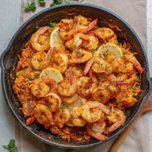 A cast iron skillet filled with cajun shrimp and rice garnished with parsley.