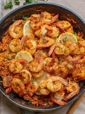 A cast iron skillet filled with cajun shrimp and rice garnished with parsley.
