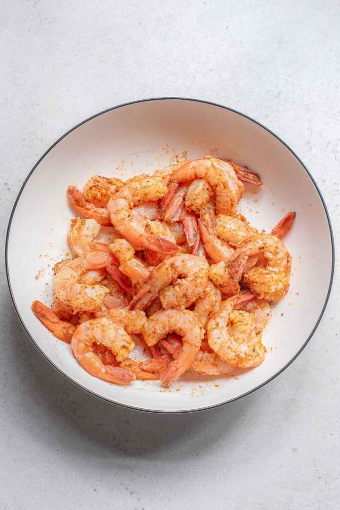 A white bowl filled with cooked, seasoned shrimp.