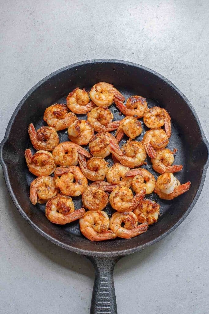 Cooked shrimp seasoned and arranged in a single layer in a black cast iron skillet.