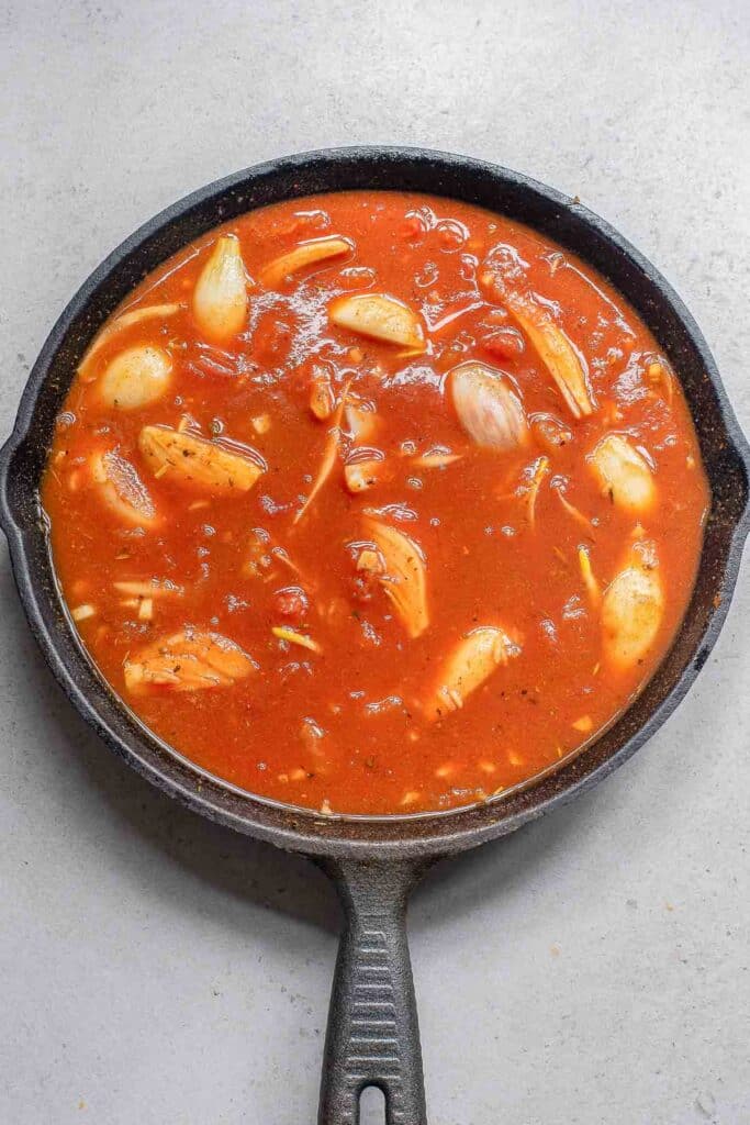 A black cast iron skillet filled with tomato-based sauce with chicken broth with diced tomato and tomato paste added in.
