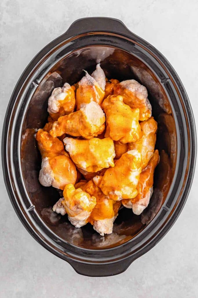 Raw chicken wings coated in a hot honey sauce inside a black slow cooker.